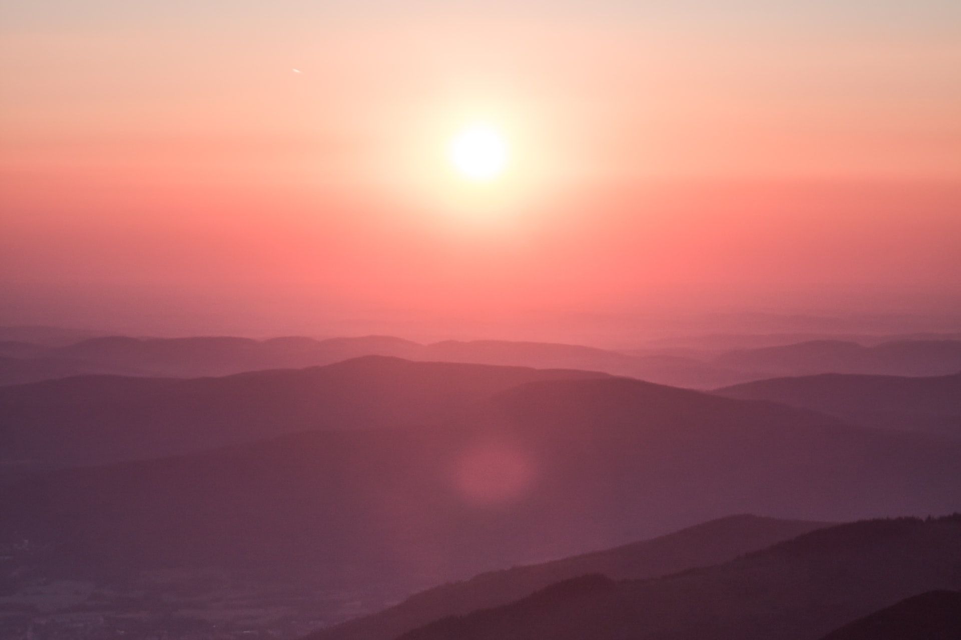 Eine rote Sonne im Hintergrund mit roten Hügeln, die in Nebel gehüllt sind.