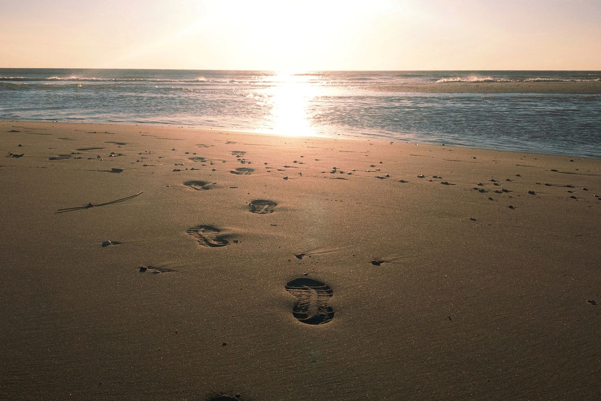 Sonnenaufgang am Strand mit Schuhabdrücken auf dem Weg zum Strand.